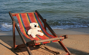 white bear plush on brown wooden folding lounger chair near seaside