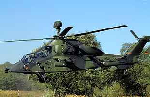 green and black camouflage attack helicopter near tree under blue sky during daytime
