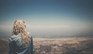 blonde haired girl standing on mountain peak during daytime