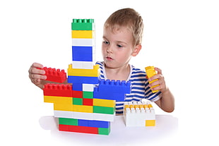 boy in blue and white striped t-shirt playing plastic building blocks toy