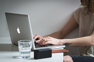 woman in white shirt using MacBook Pro near on clear drinking glass
