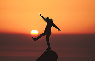 silhouette photo of a person standing on stone during golden hour