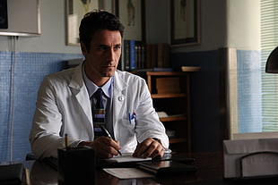 man in white dress shirt holding pen sitting on chair beside desk in room