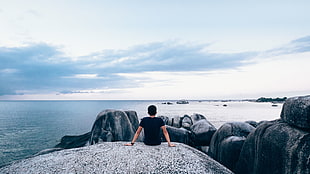person sitting on gray stone cliff during day time HD wallpaper