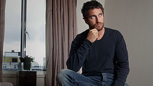 man wearing white sweatshirt and denim jeans sitting near at the brown window curtain HD wallpaper