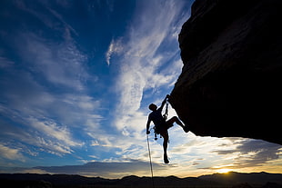 silhouette of man climbing on mountain during daytime