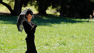 woman in black long-sleeve dress while holding umbrella on green grass field during daytime
