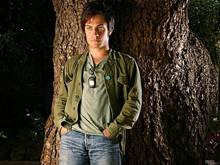 man wearing green jacket standing near tree