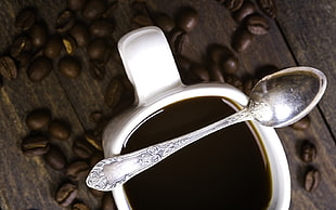 stainless steel spoon on top of white ceramic mug surrounded with coffee beans