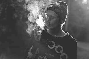 grayscale photo of man wearing crew-neck tops smoking
