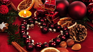 christmas baubles placed on red surface shaped as heart beside nuts and tinsel