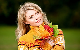 photo of woman wearing brown turtle neck sweater holding maple leaf