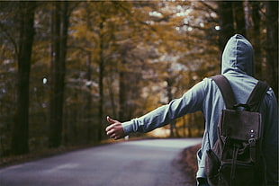 person in gray hoodie wearing backpack standing on asphalt road