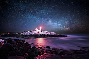 white concrete lighthouse surrounded by body of water under starry night