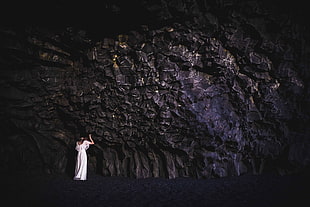 woman wearing white dress standing in front of stone cave
