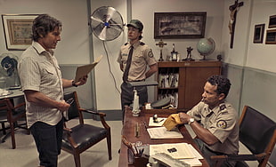 man in white button up shirt holding documents in front of police officer sitting on beside brown wooden desk