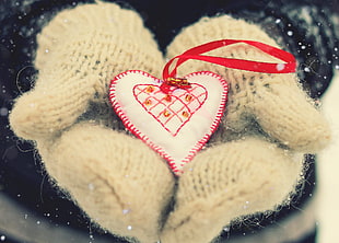 person wearing white winter gloves holding white and red heart ornament
