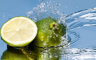 green sliced lemon pouring water in closeup photography