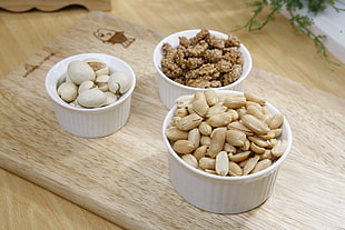 three bowls of nuts, eggs, and sweets on chopping board