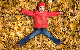 boy wearing red zip-up jacket lying down on bed of dried maple leaves