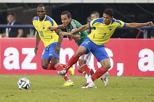 man in green shirt in between of two man in yellow shirt playing soccer
