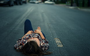 shallow focus photography of black haired woman lying on gray asphalt rode