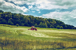 red tractor operating on green grass field during daytime