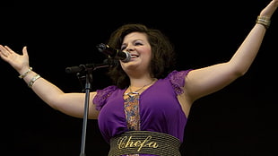 woman in purple blouse and brown Chefa belt standing in front of microphone with stand