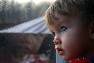 blond haired toddler looking outside glass window during daytime HD wallpaper