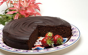 sliced chocolate cake and three strawberries on round white and pink floral plate