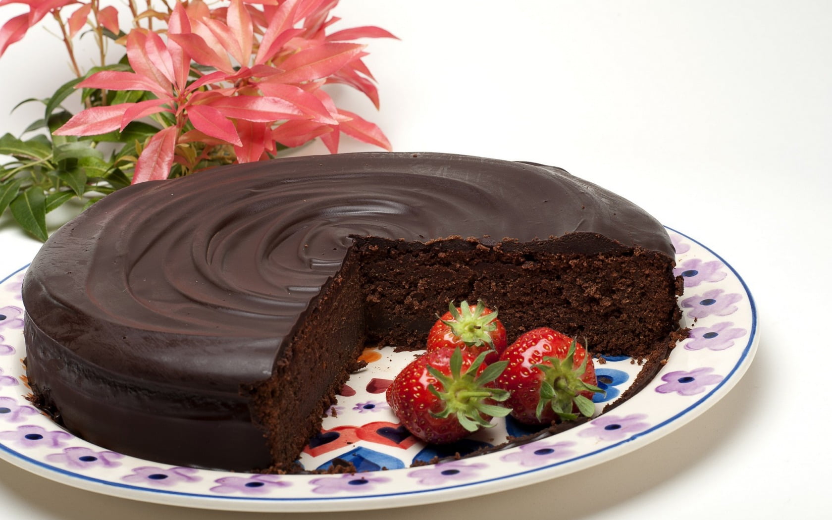 sliced chocolate cake and three strawberries on round white and pink floral...
