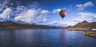 hot air balloon on sky above body of water under blue sky HD wallpaper