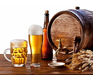 clear beer mug and pilsner glass beside brown glass bottle and brown wooden barrel on table