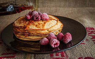 pancake with raspberry on round brown plate with maple syrup