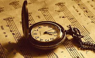 sepia photography of pocket watch on top of music note