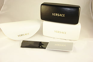 two white and one back Versace sunglasses cases on white textile