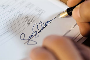 close-up photo of person writing signature on paper