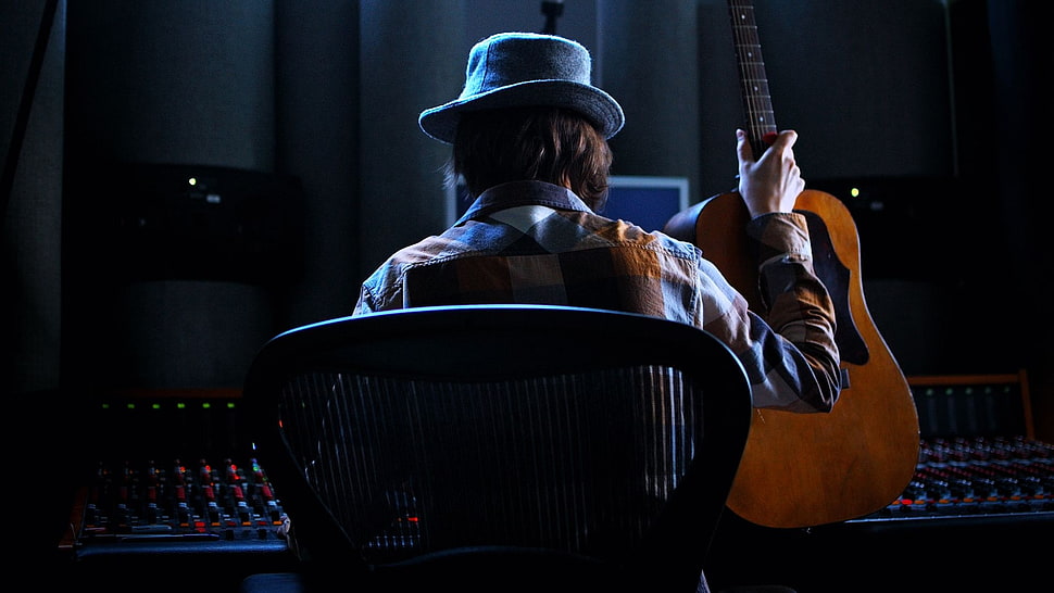 man in blue hat holding guitar while sitting HD wallpaper