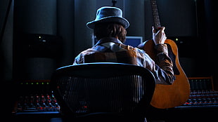 man in blue hat holding guitar while sitting