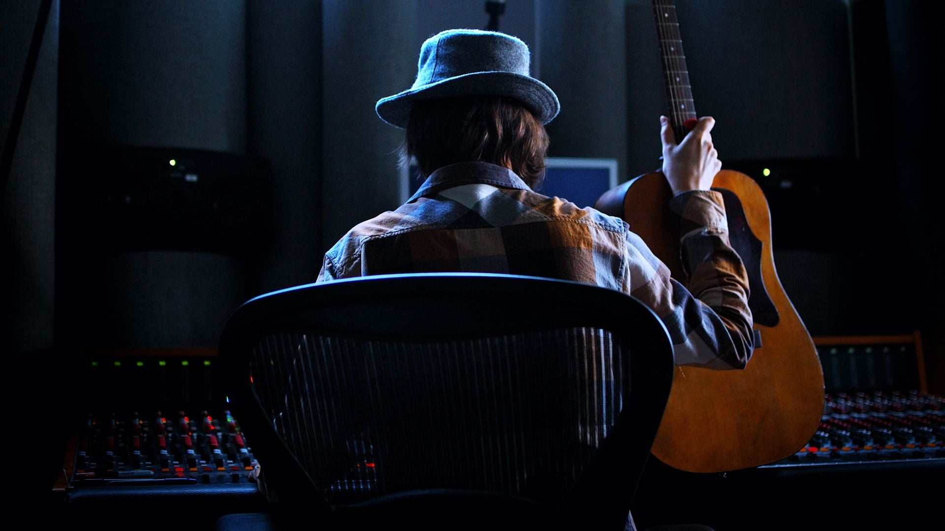 man in blue hat holding guitar while sitting