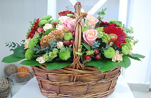bouquet of pink, green and red flowers in brown woven basket