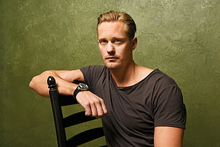 close up photo of man wearing black scoop-neck top resting his arms on chair