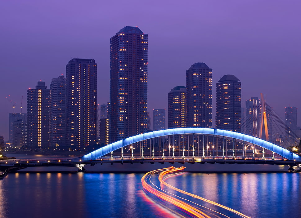 suspension bridge near high rise buildings during nighttime HD wallpaper