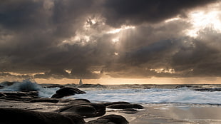landscape photography of seashore with small seawaves under crepuscular rays and nimbus clouds