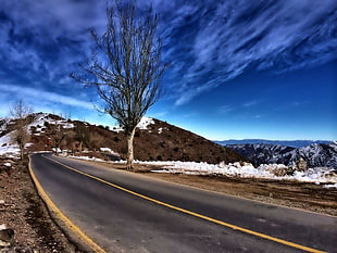 gray concrete long road beside rocky mountains coated with snow under blue and white sky, chile