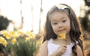 selective focus photography of girl holding yellow petaled flower
