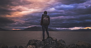 landscape photography of a person carrying brown backpack standing in mountain peak during golden hour