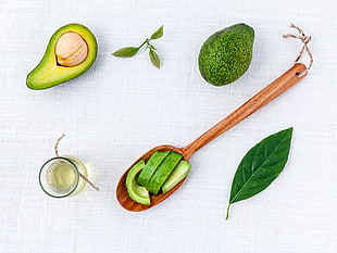 food photography of sliced avocados on spatula beside leaves and avocado
