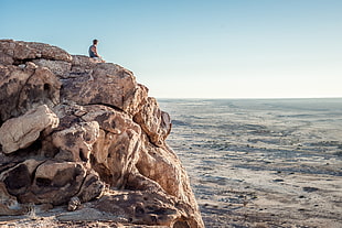 man sitting on rocky mountain during daytime HD wallpaper