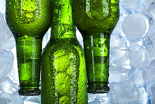 three green glass bottles on top of ice